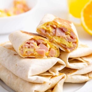 A plate of ham and cheese burritos with one split in half.