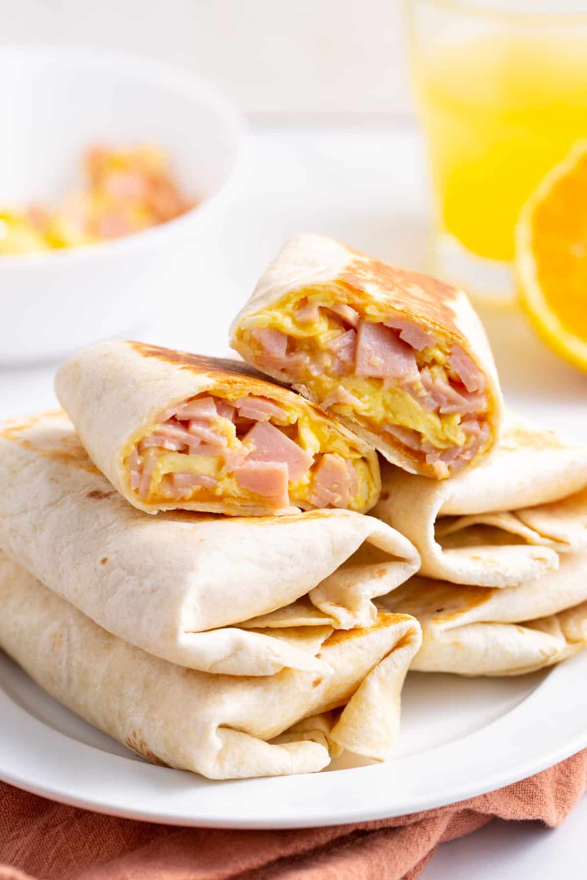 ham and cheese burritos cut in half and stacked on other burritos served on a white round plate.