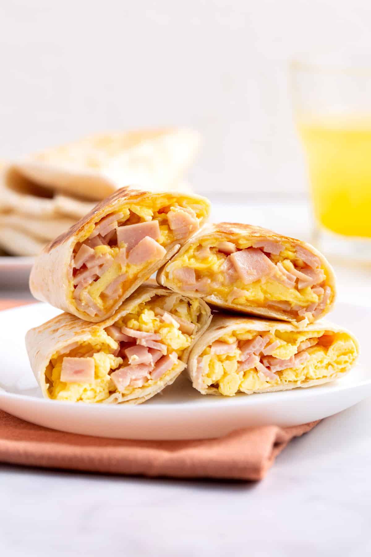 two ham and cheese breakfast burritos cut in half and stacked on a white round plate