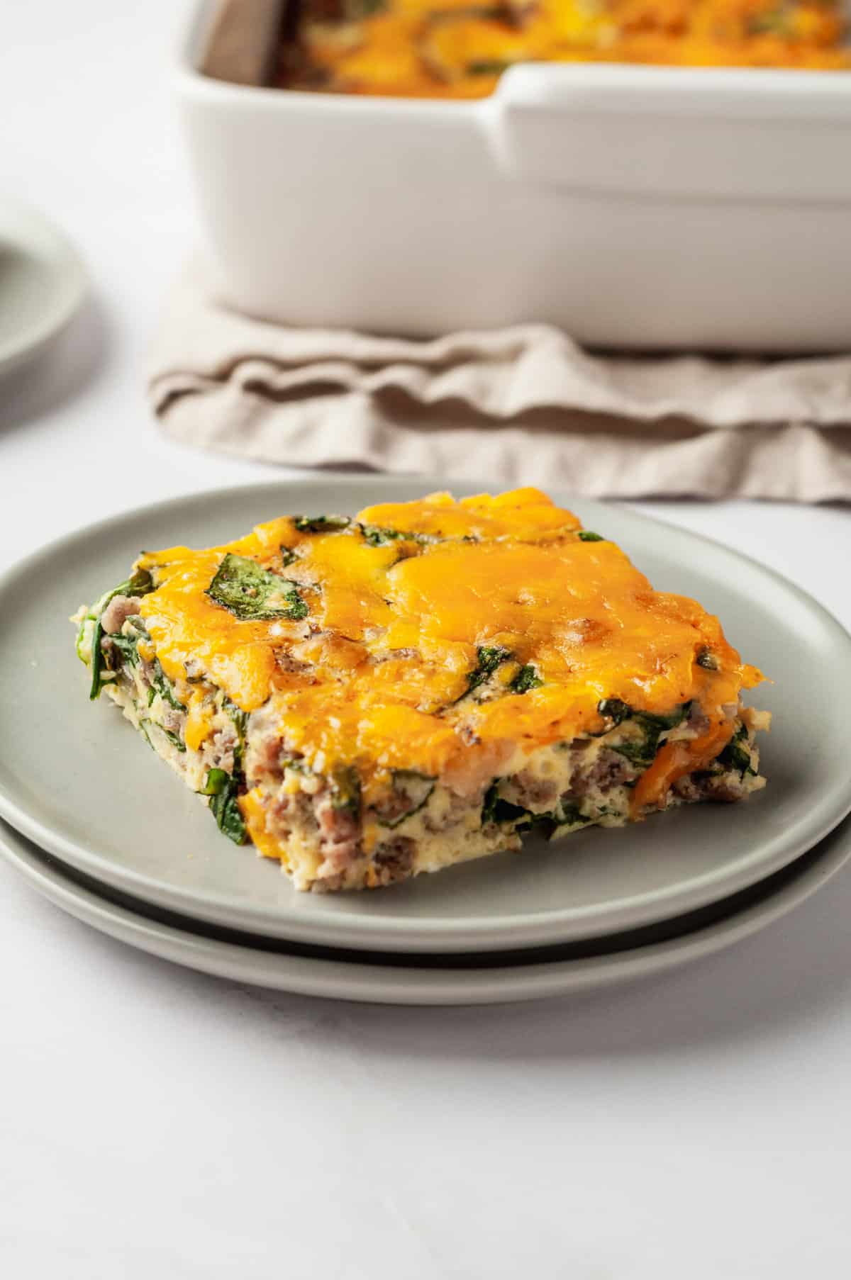 close up image of a square serving of keto breakfast casserole sitting on a grey round plate