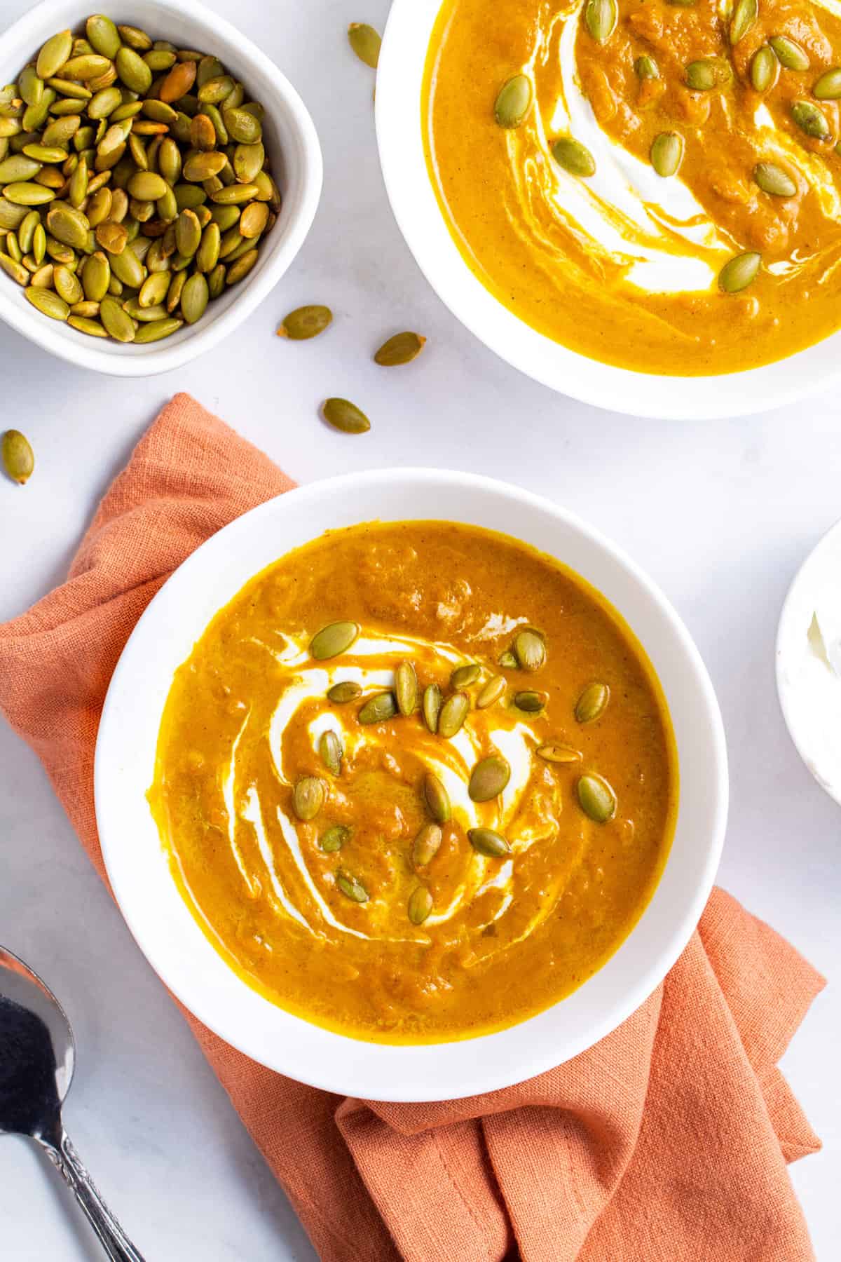 top down image of two bowls pumpkin soup served in a white round bowl with a side of roasted pumpkin seeds