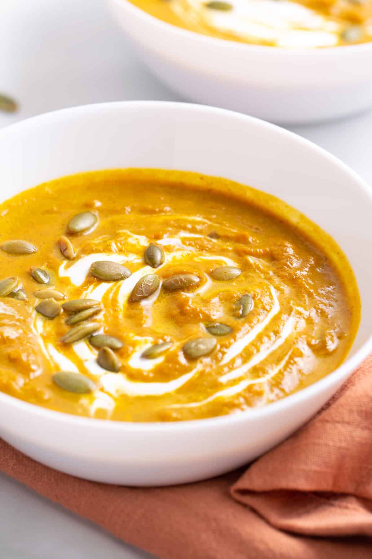 close up of a bowl of pumpkin soup served in a white round bowl
