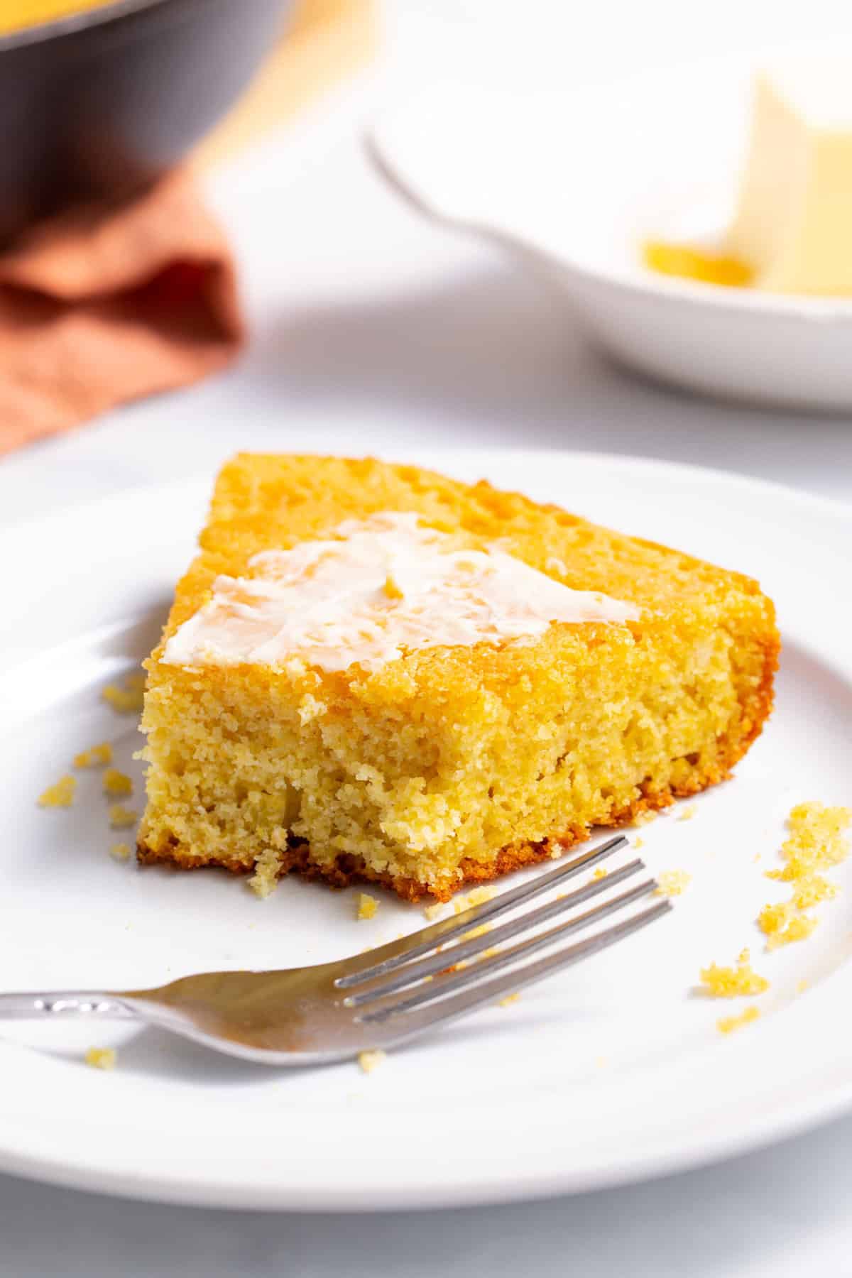serving of skillet cornbread topped with butter and served on a white round plate with a silver fork