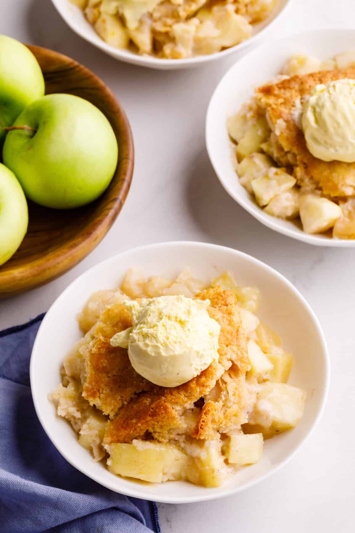 top down image of apple cobbler with a scoop of vanilla ice cream served in a white round bowl