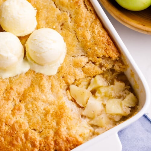 A dish of apple cobbler topped with three scoops of vanilla ice cream.