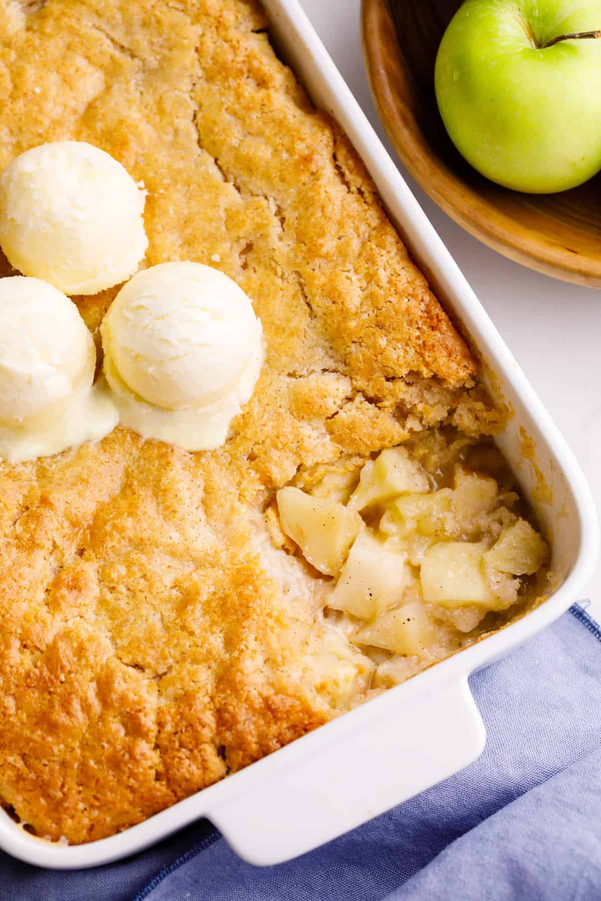 Apple cobbler served in a casserole dish topped with three scoops of vanilla ice cream.