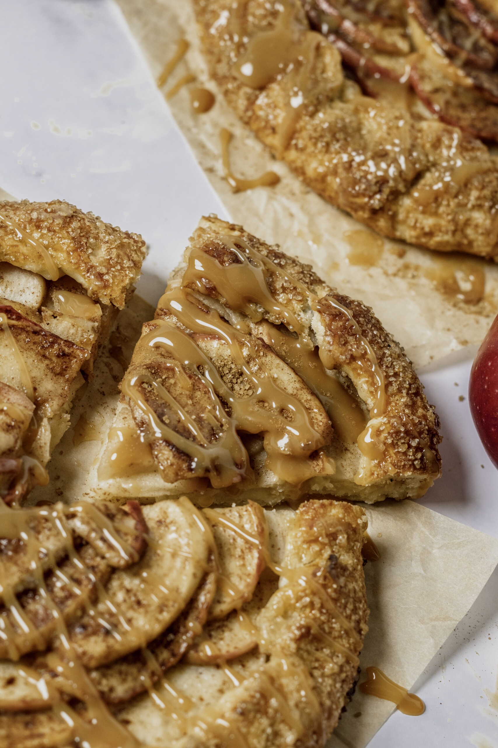 close up image of a slice of apple galette sitting on parchment paper with the remaining apple galette.