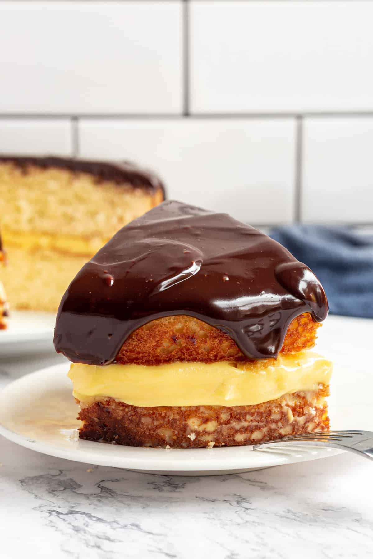 slice of boston cream pie cake showing the layers and served on a white round plate