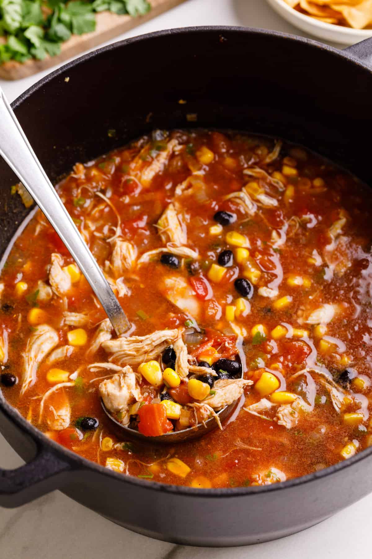 cast iron dutch oven serving chicken tortilla soup with a ladle