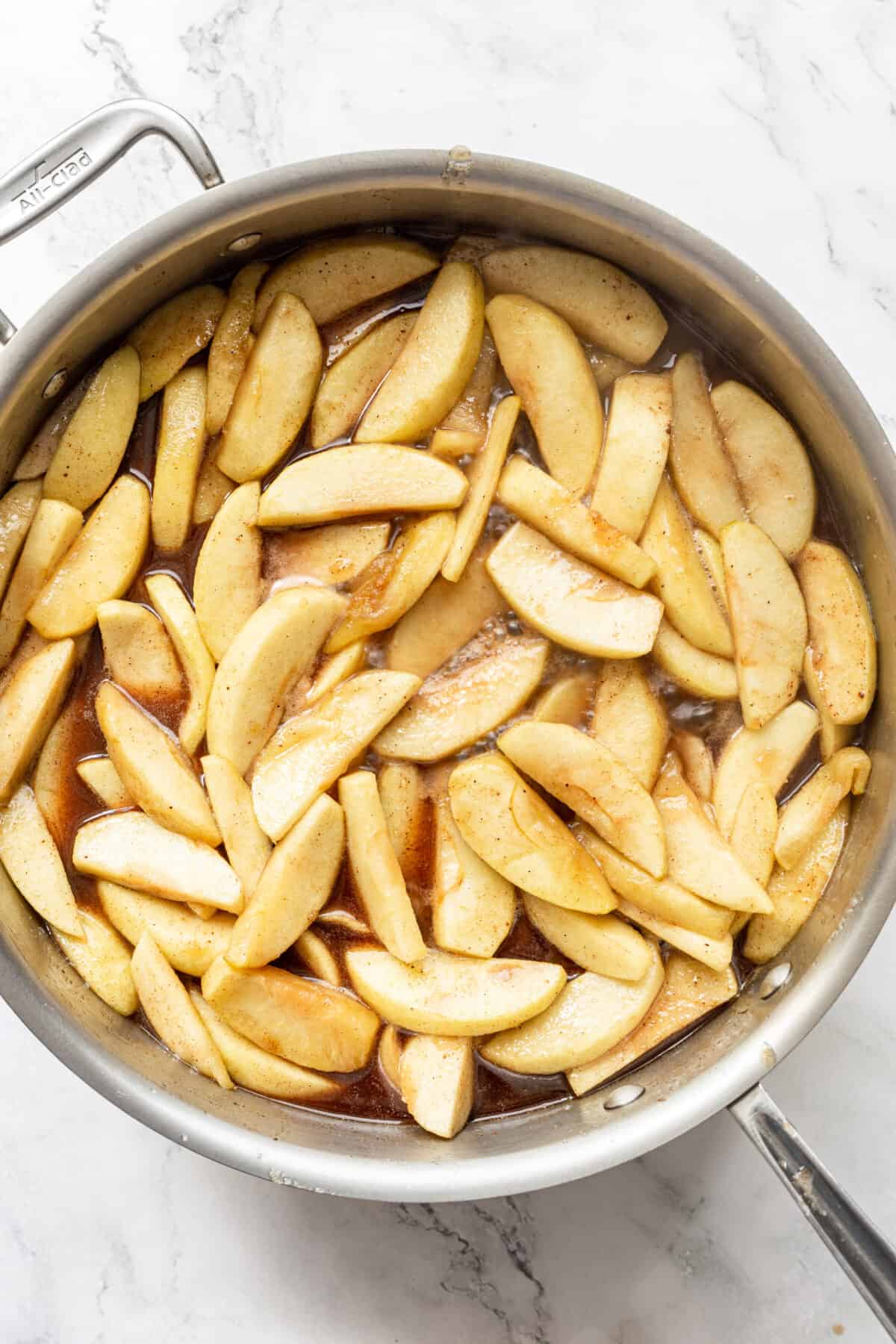 A top down shot of a pan full of sliced apples cooking in butter.
