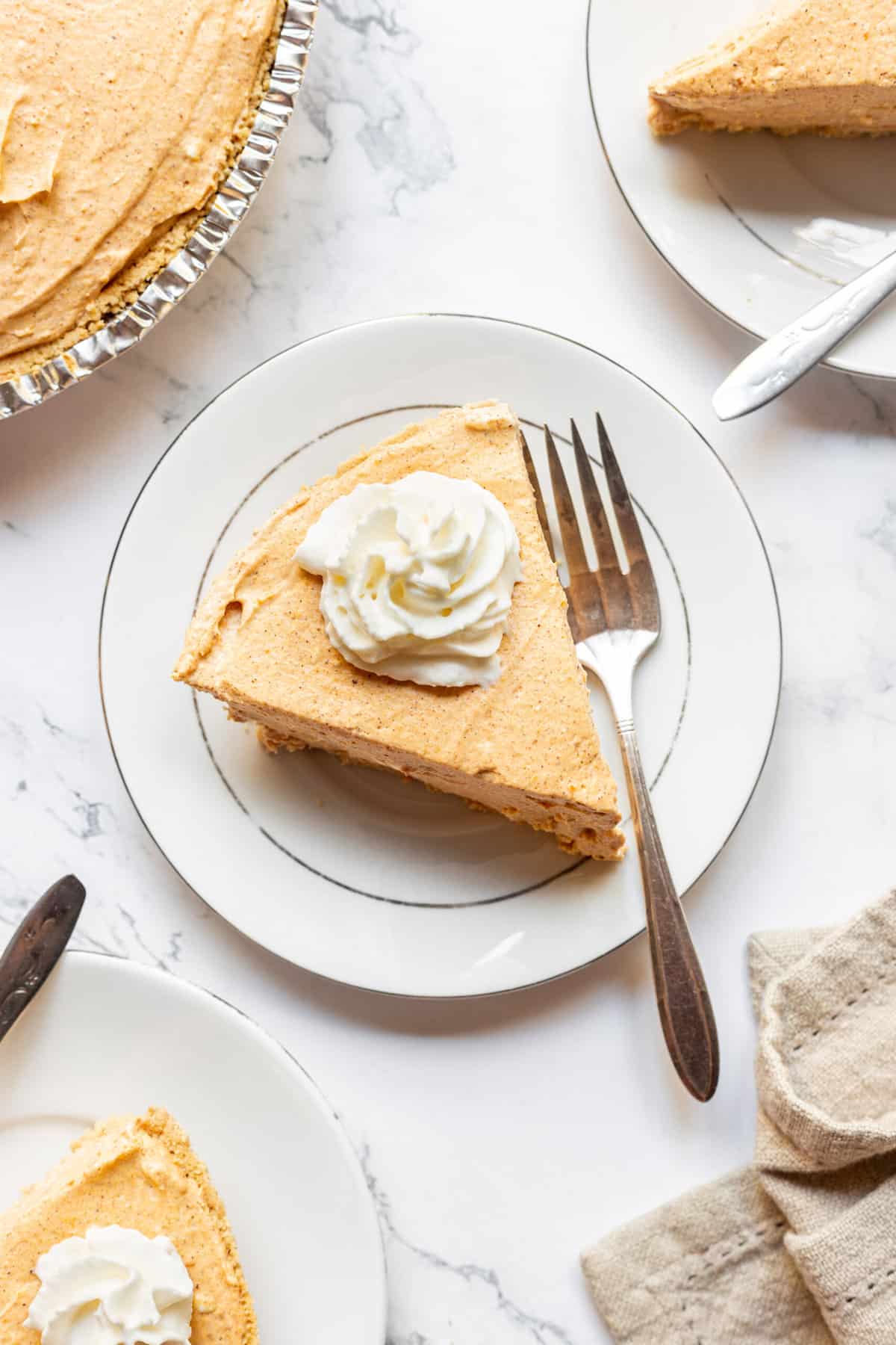 top down image of a slice of pumpkin cheesecake served on a white round plate with a silver fork