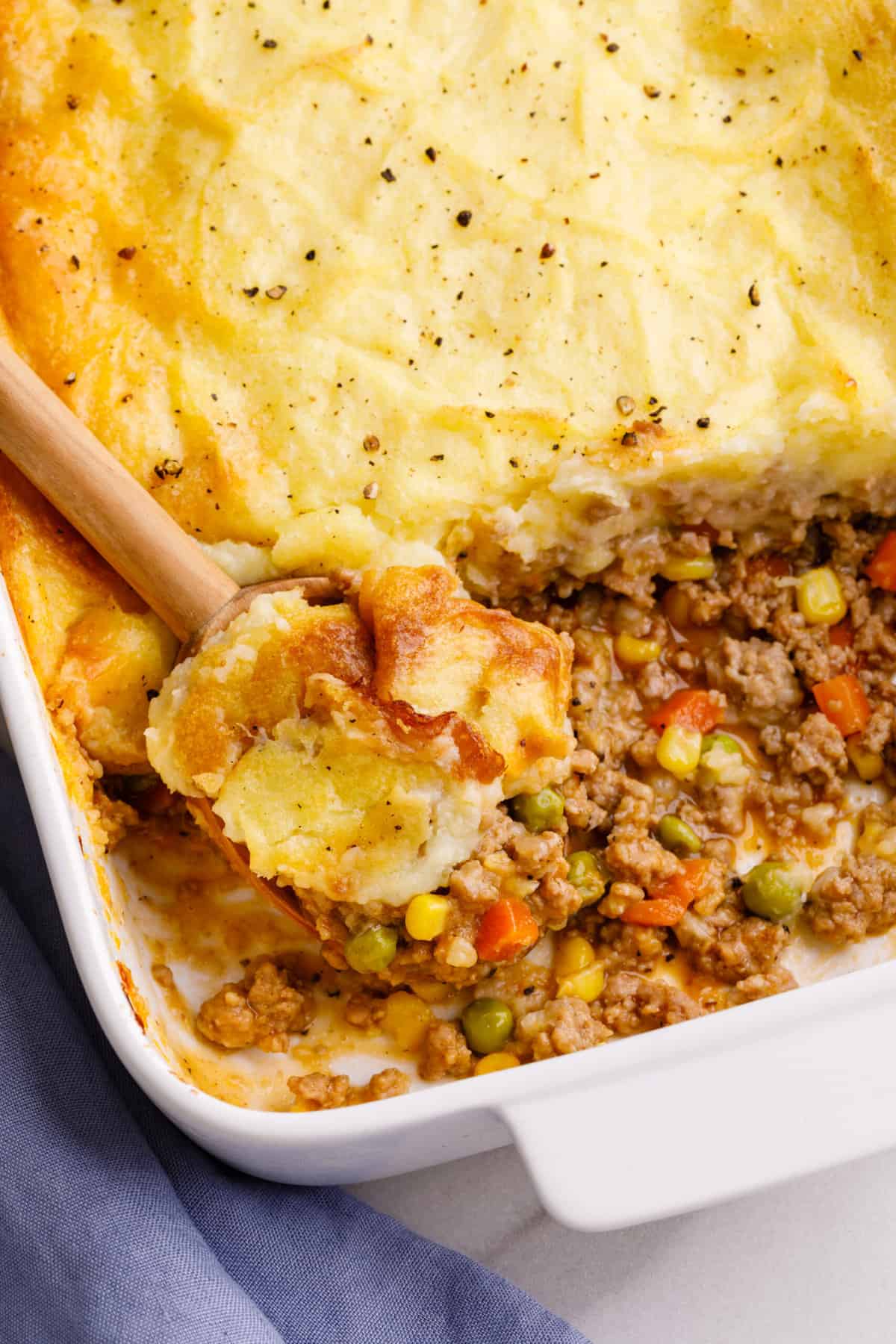 Close up image of shepherd's pie served in a casserole dish with a wooden spoonful of the pie.
