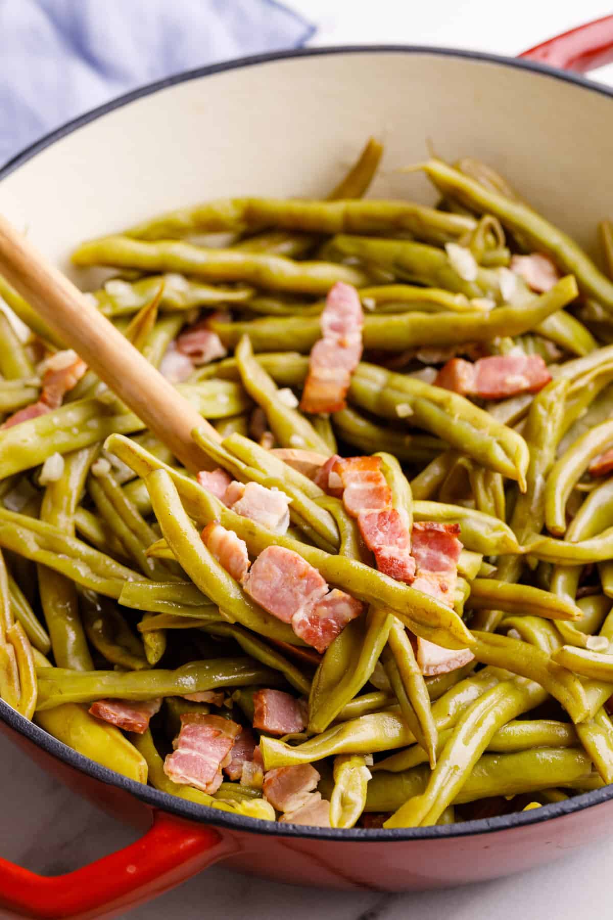 close up image of southern style green beans in a dutch oven with a wooden spoon