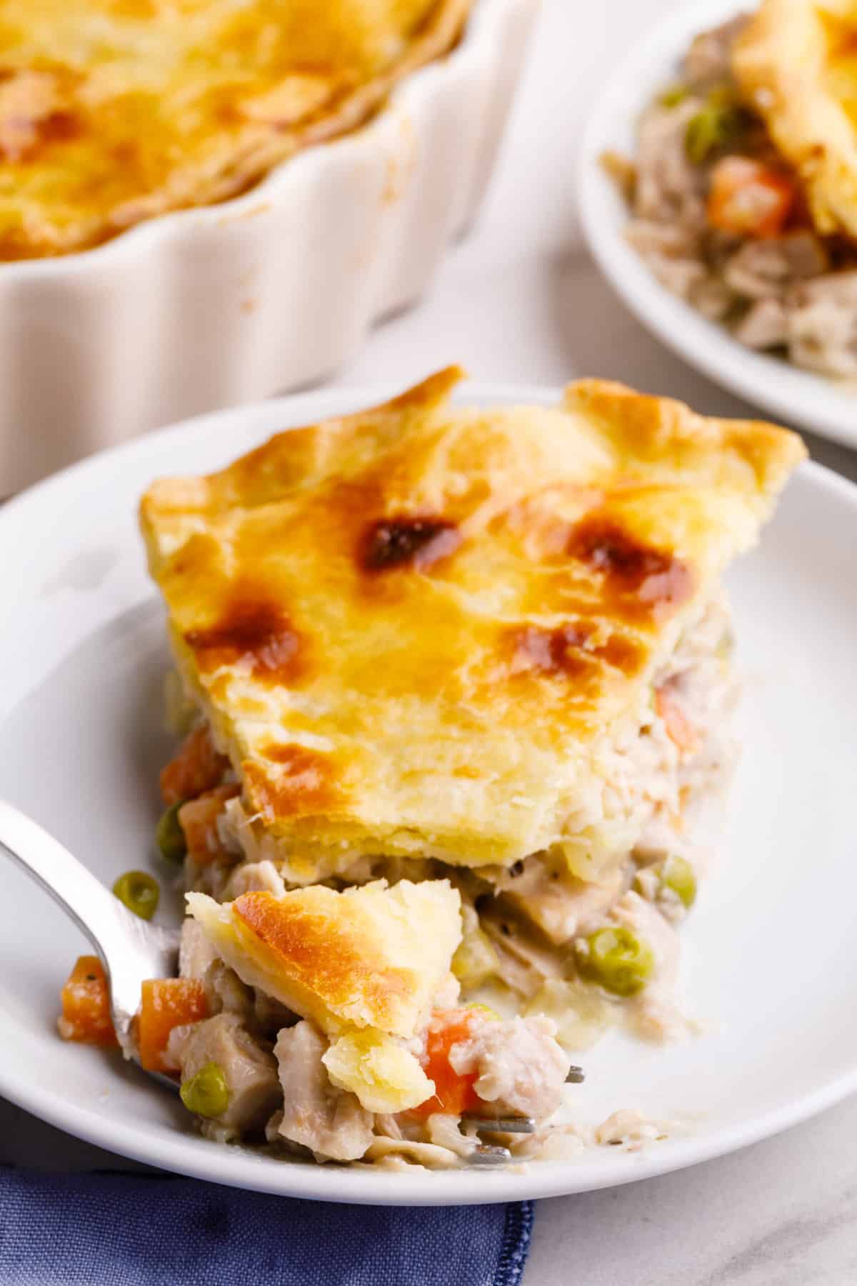slice of turkey pot pie with a forkful of pie served on a white round plate.