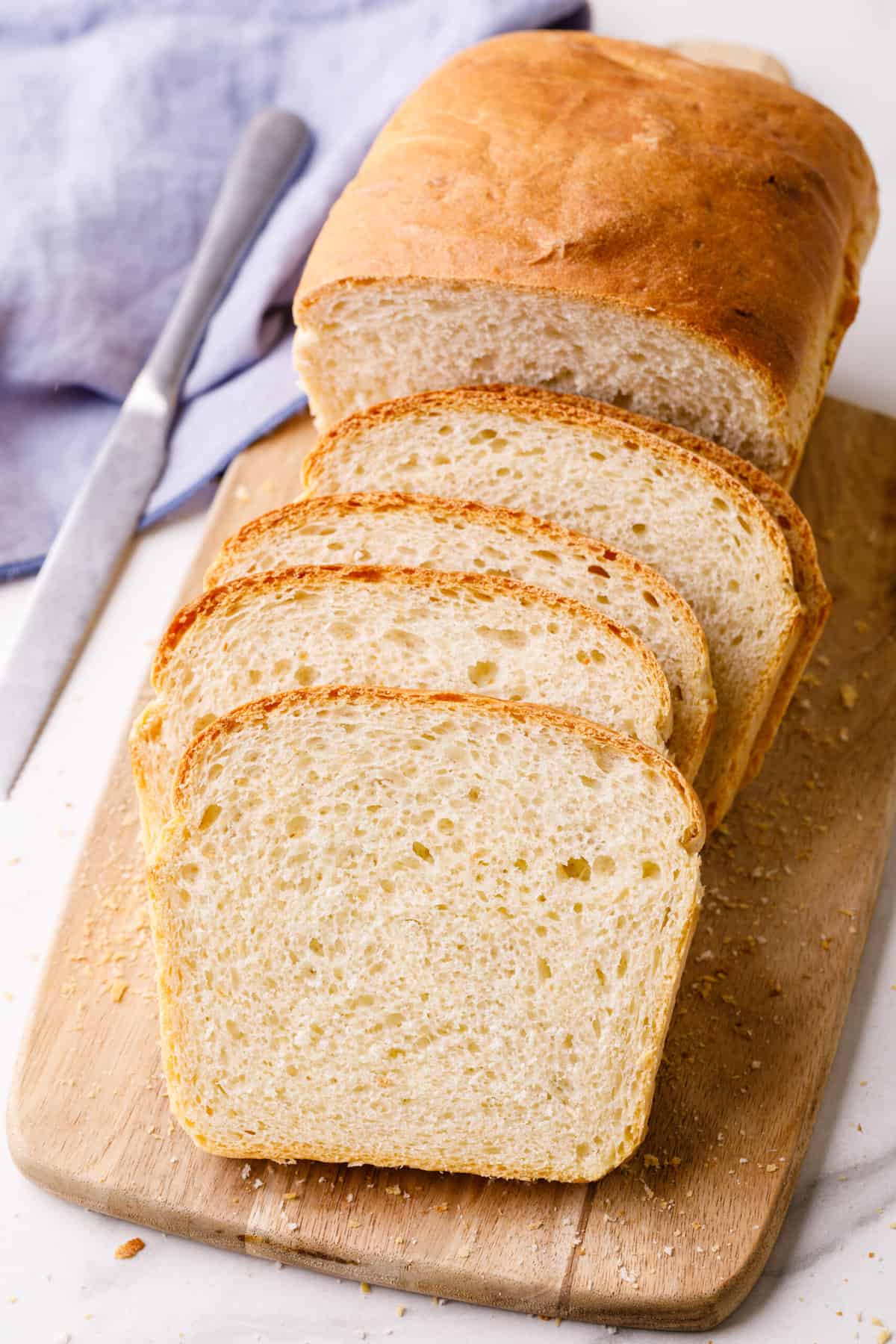 sliced homemade white sandwich bread sitting on a wooden cutting board.