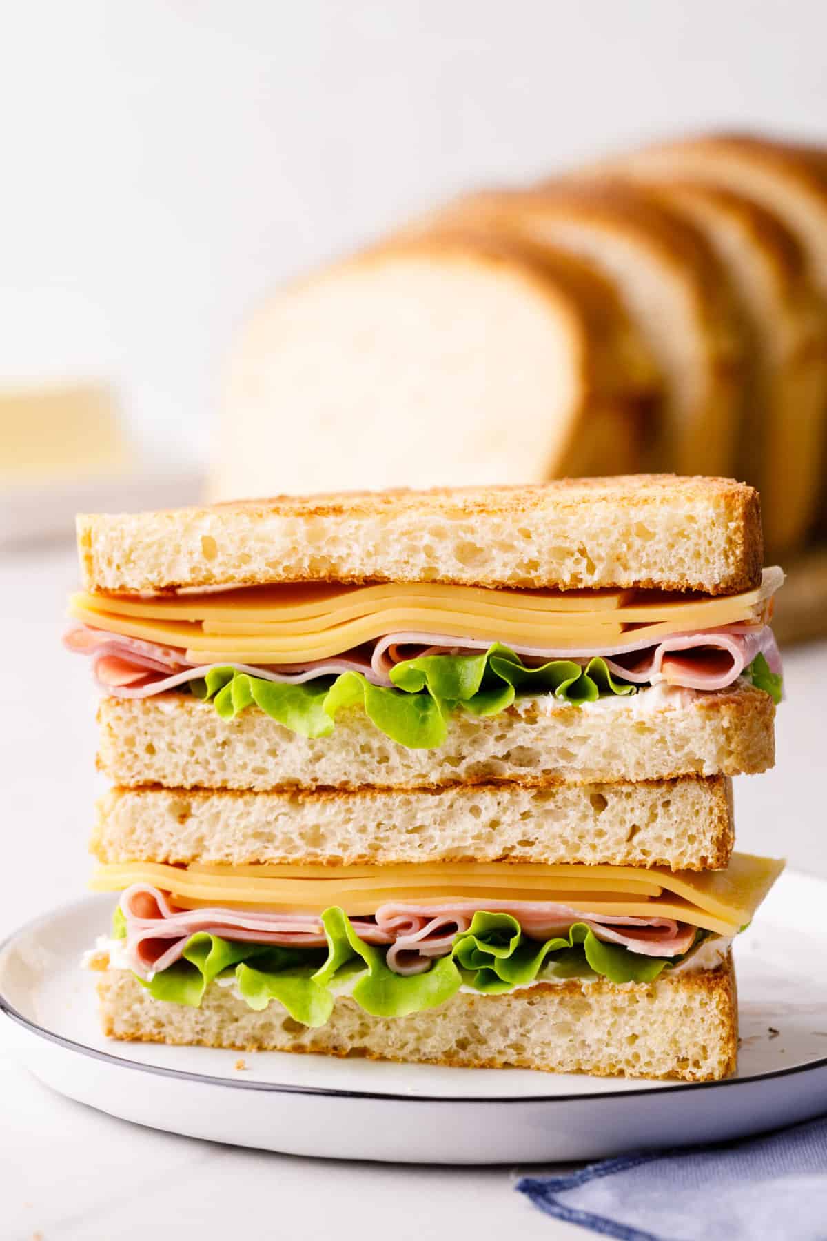 ham and cheese sandwich made with homemade white sandwich bread cut in half and stacked sitting on a white round plate