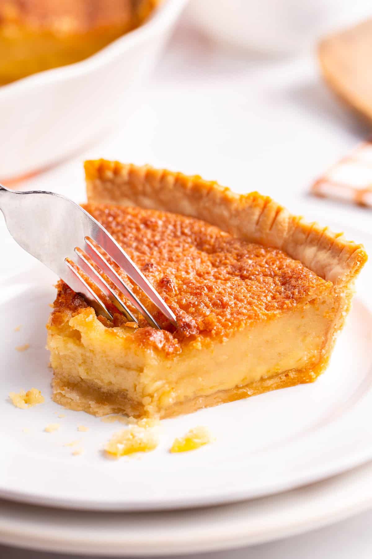 fork digging into a slice of chess pie served on a white round plate
