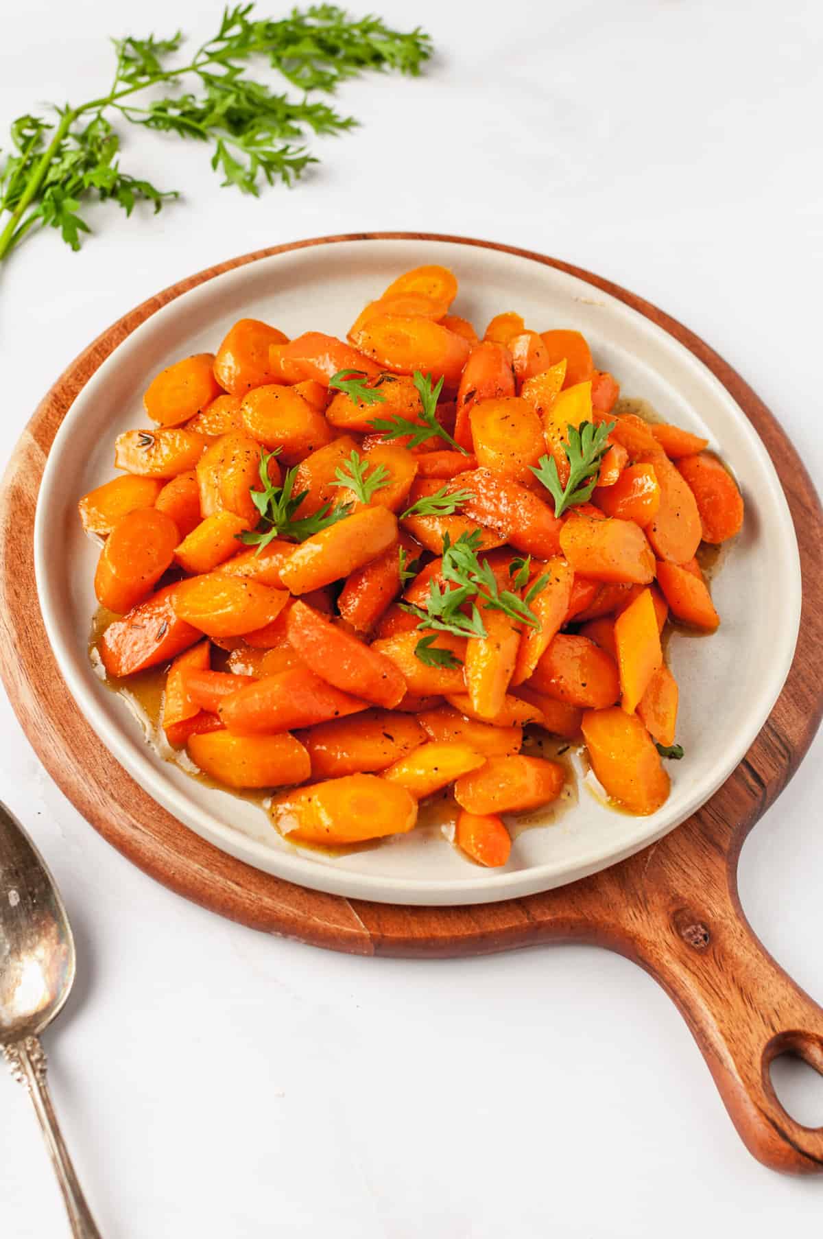 close up image of honey glazed carrots served on a grey round plate with a silver fork.