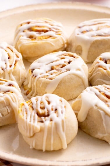 A plate of pumpkin cinnamon rolls topped with cream cheese icing.