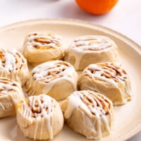 A plate of pumpkin cinnamon rolls topped with cream cheese frosting.