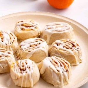 A plate of pumpkin cinnamon rolls topped with cream cheese frosting.