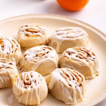 A plate of pumpkin cinnamon rolls topped with cream cheese frosting.
