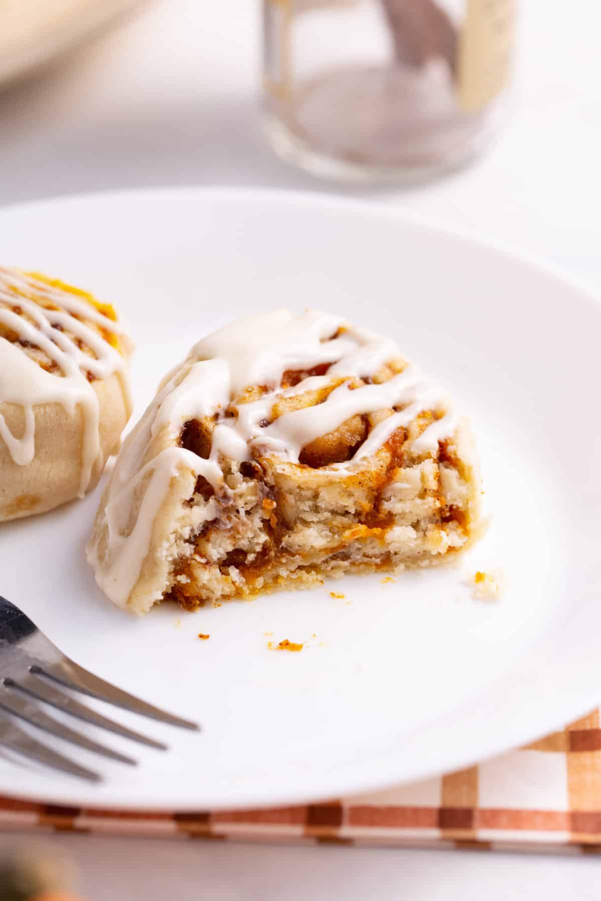 a serving of pumpkin cinnamon roll cut in half to show the cross section and served on a white round plate.