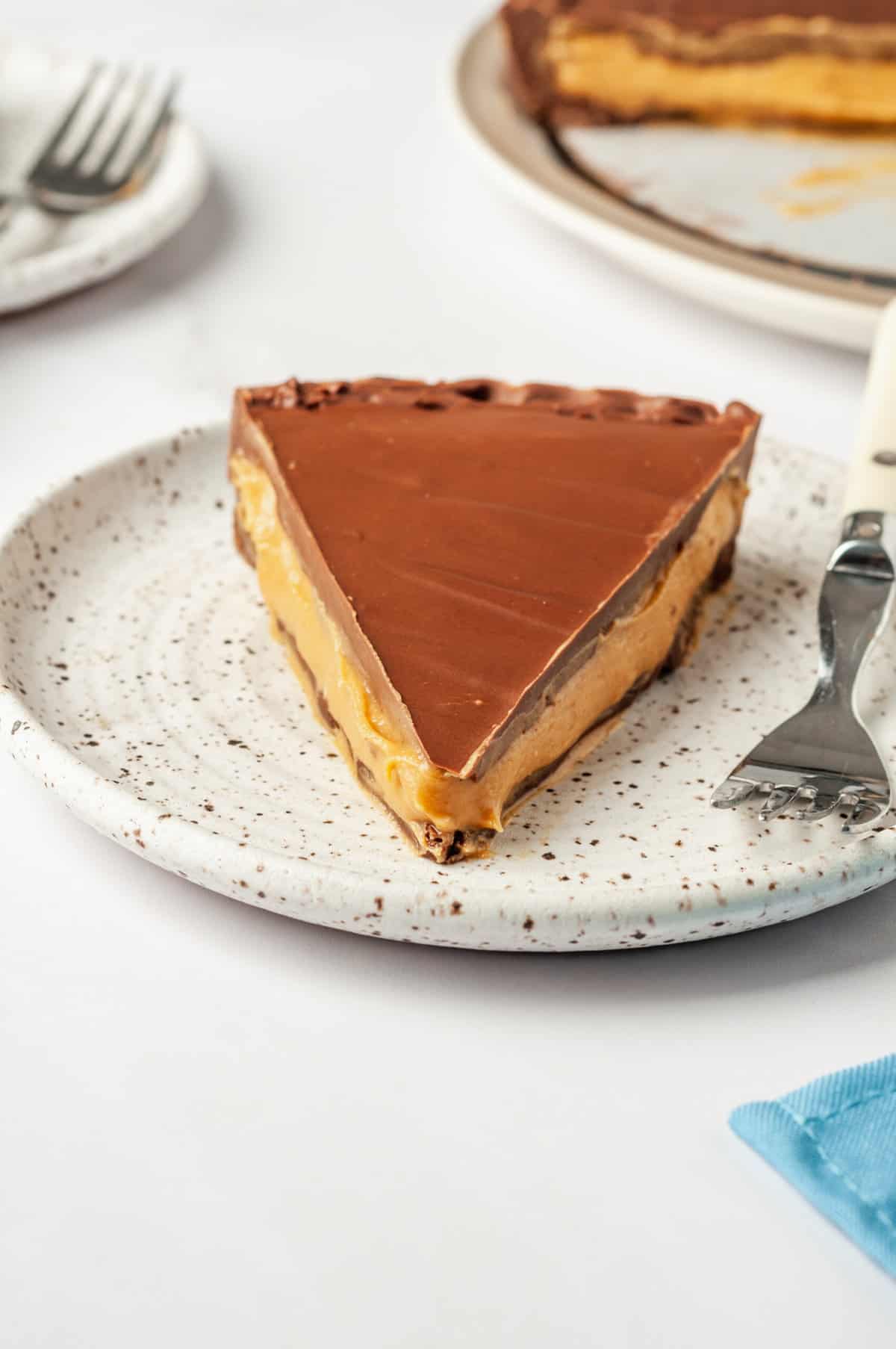S close up image of a slice of Reese's peanut butter cup pie served on a brown speckled plate with a fork next to it.