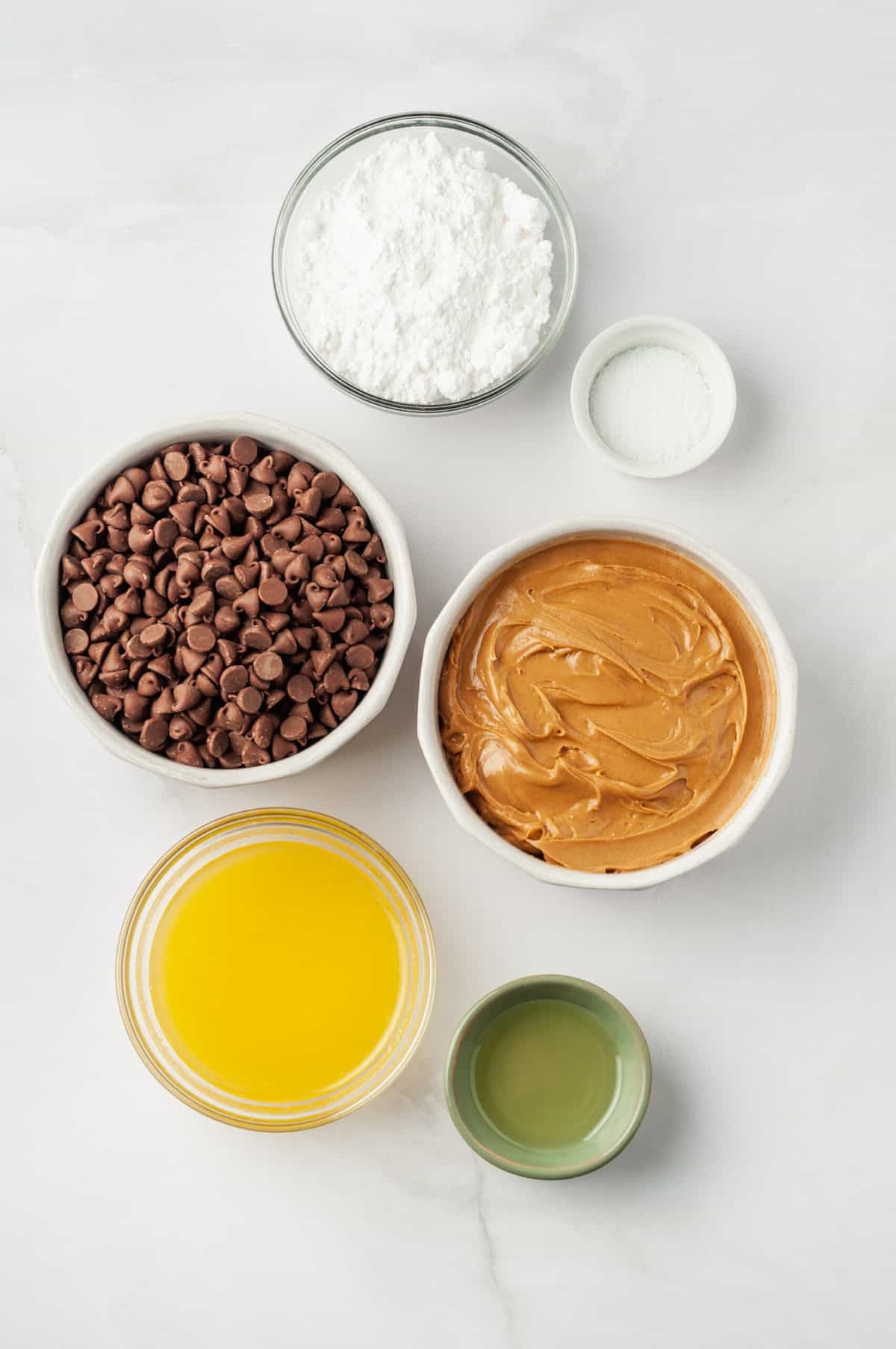 The ingredients to make Reese's peanut butter cup pie are shown portioned out on a white background: peanut butter, butter, chocolate chips, powdered sugar, salt.