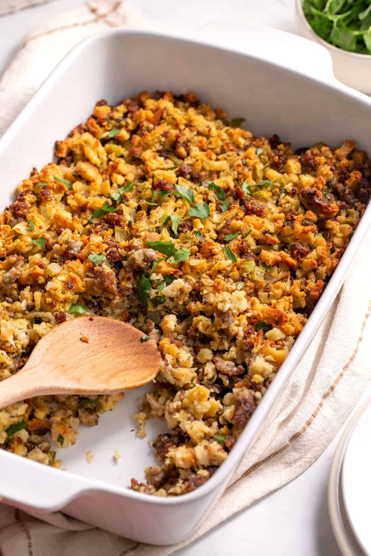 Sausage stuffing served in a white rectangle casserole dish with a wooden spoon.
