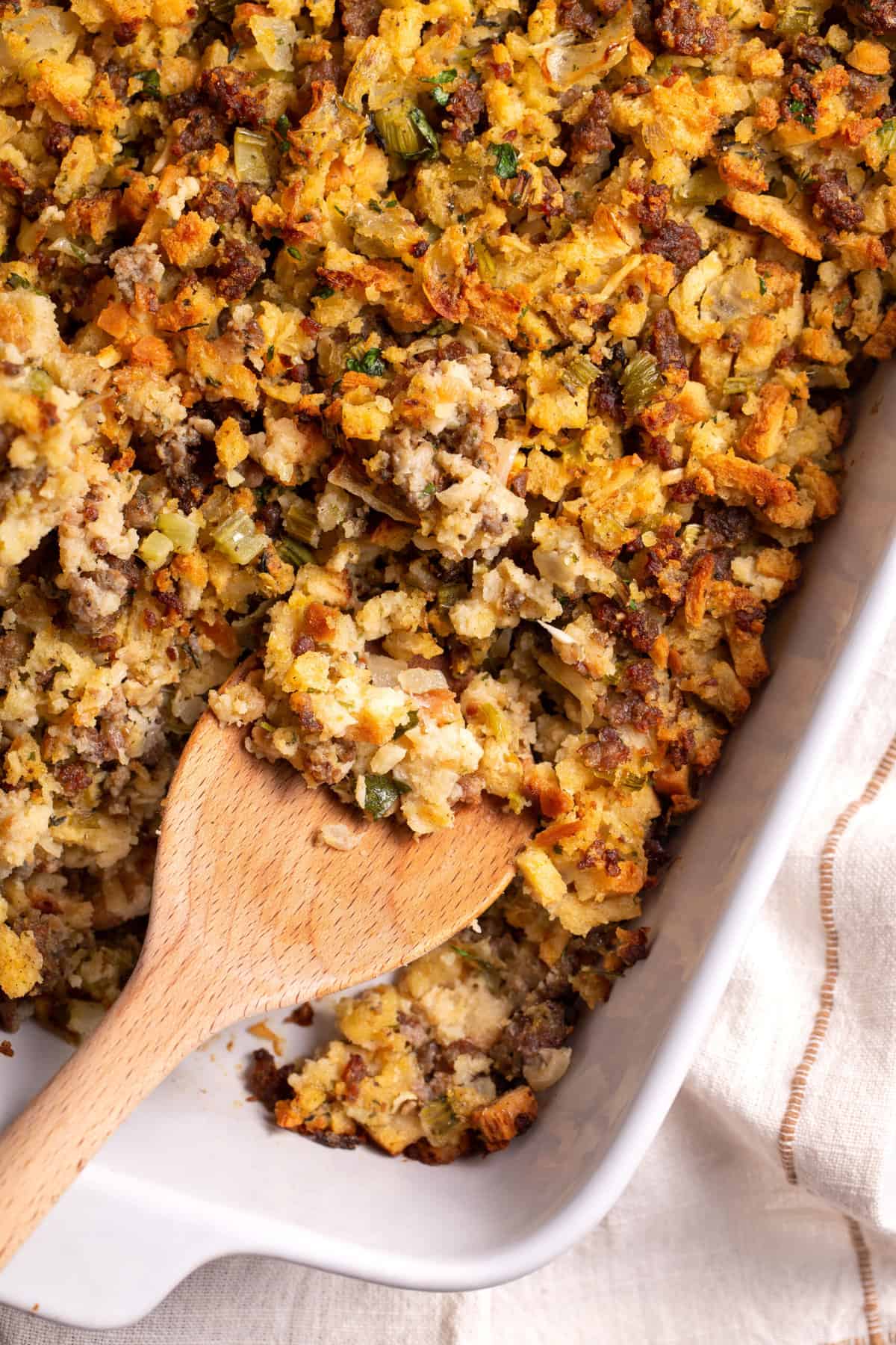 Close up of sausage stuffing served in a casserole dish with a wooden spoon.