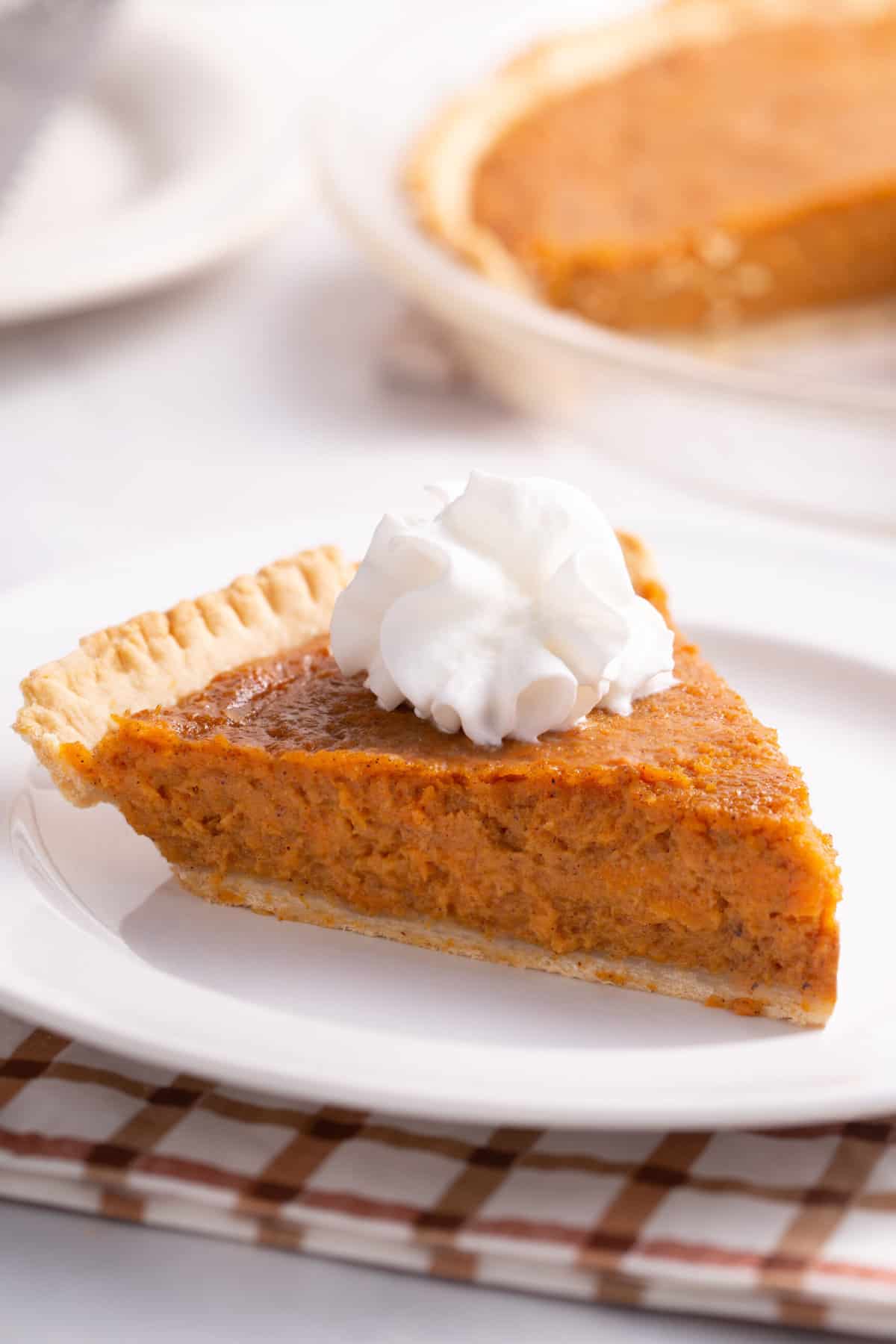 slice of sweet potato pie with a dollop of whipped cream served on a white round plate