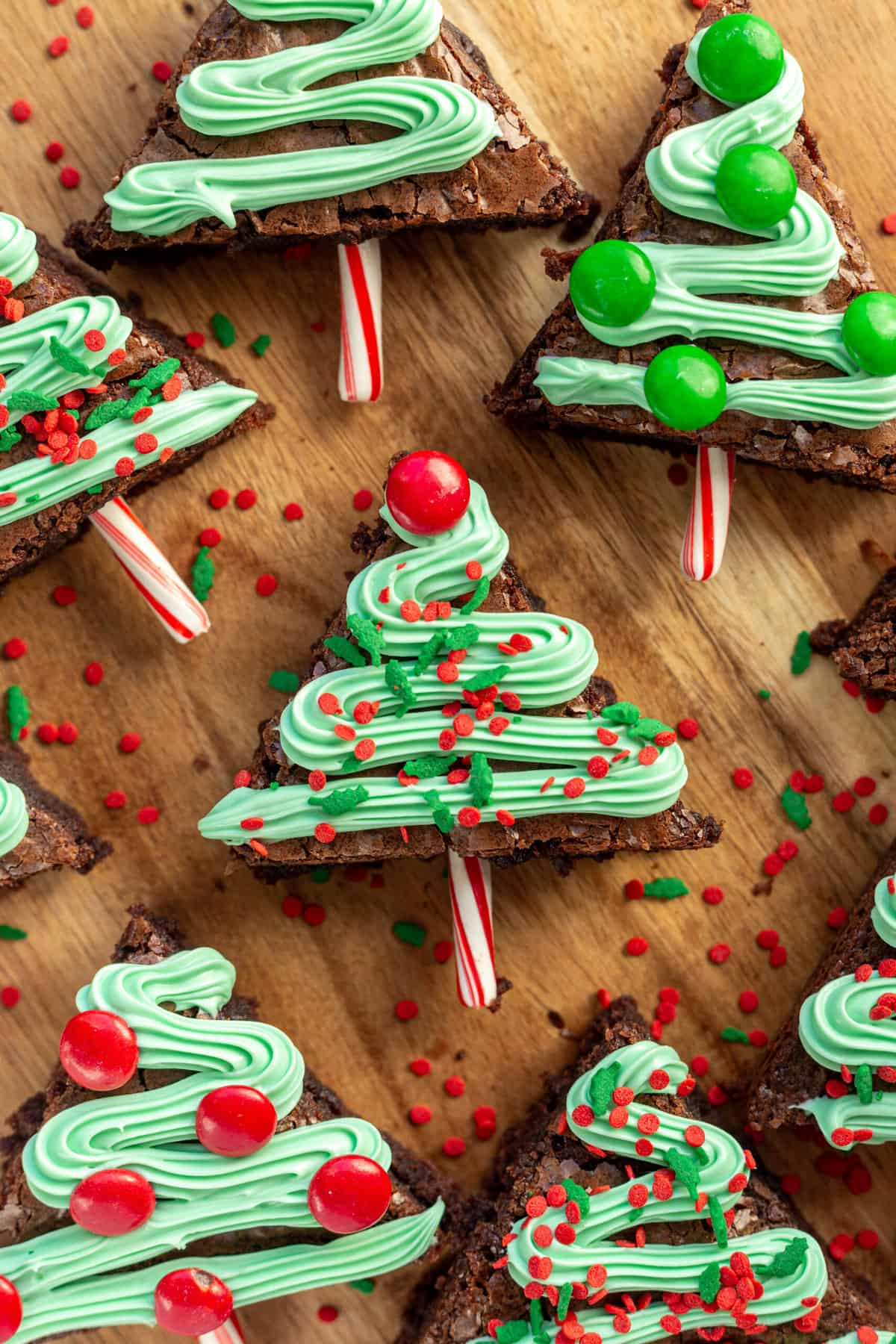 close up and top down image of christmas tree brownies with garland green frosting and red and green sprinkles with M&Ms and candy cane sticks for decoration