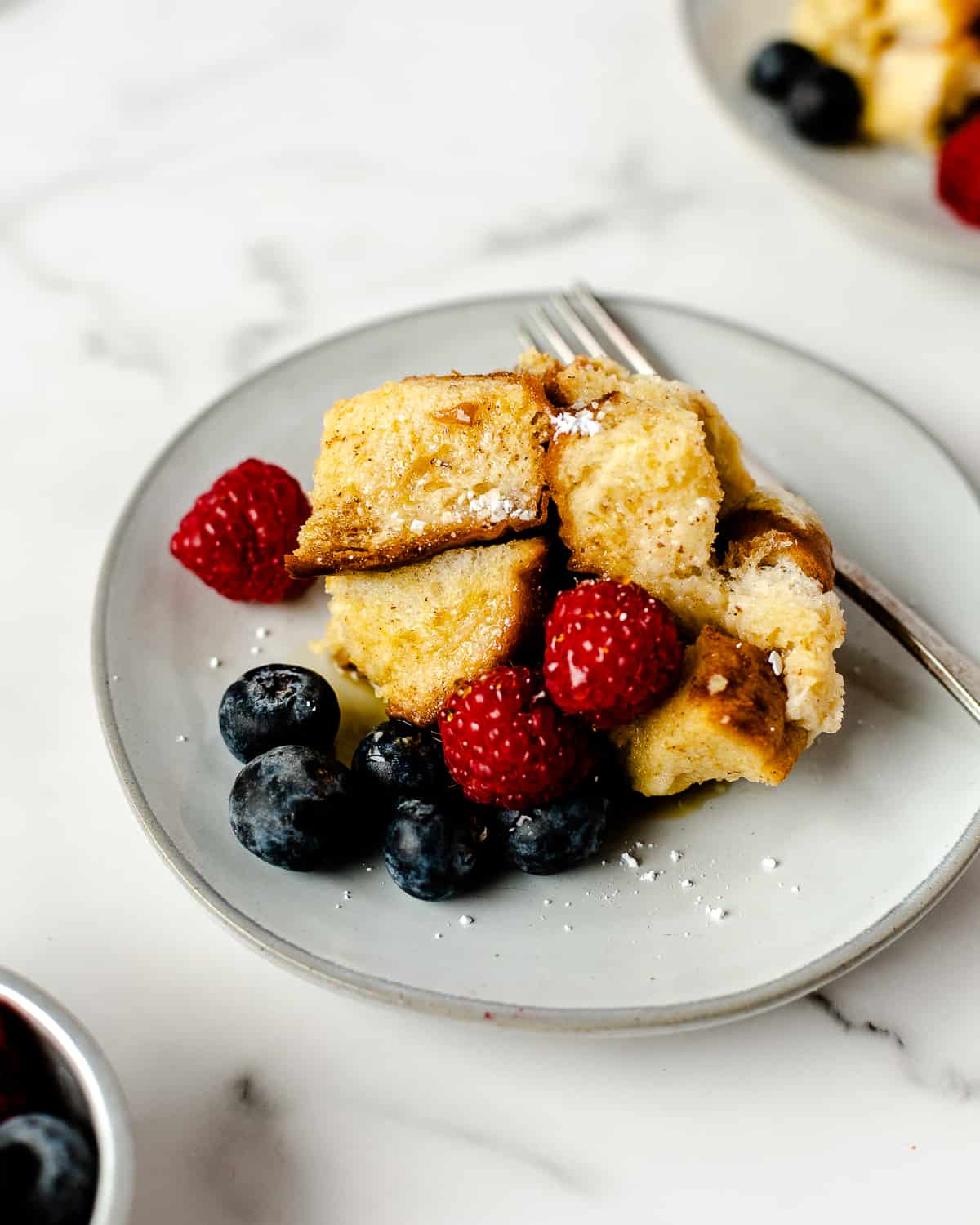 close up image of a serving of crockpot french toast casserole with fresh berries served on a grey round plate with a silver fork
