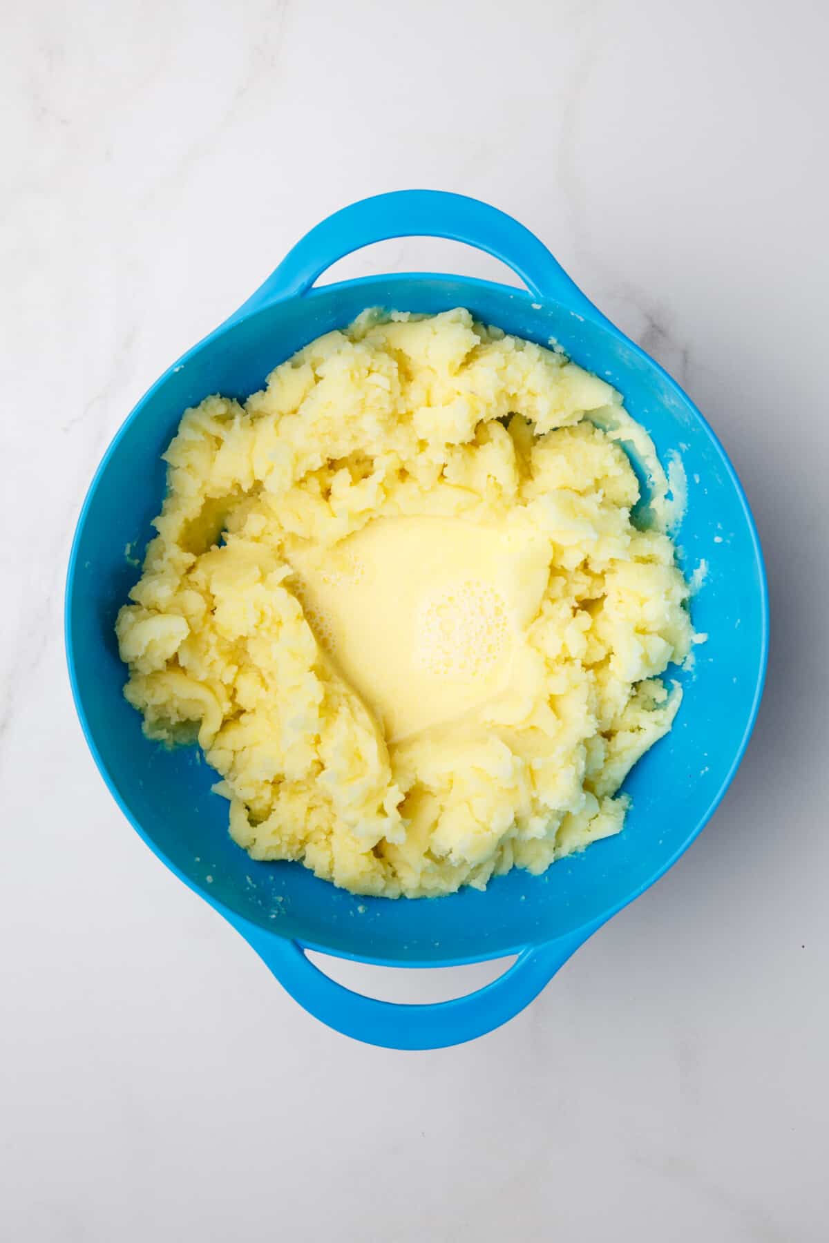 Warm butter and milk added to mashed potatoes in bowl.