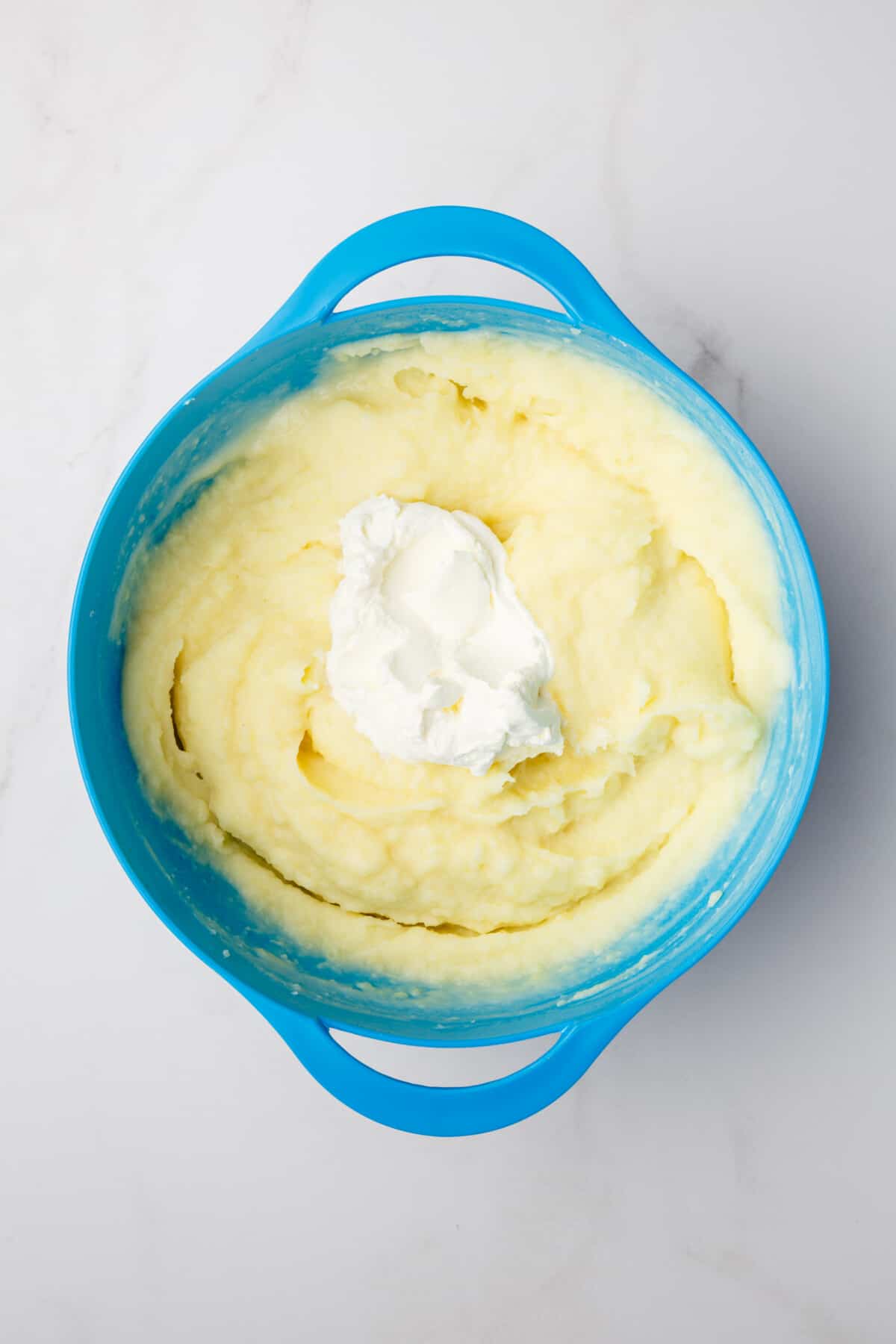 Sour cream added to mashed potatoes in bowl.