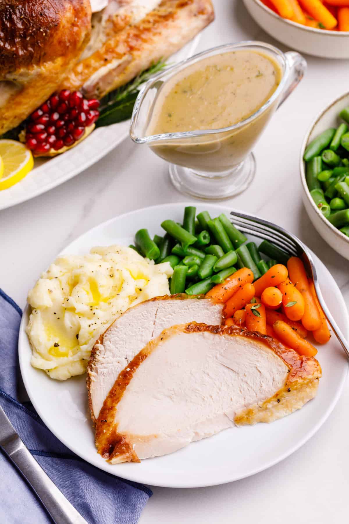 plate of two roasted turkey servings, carrots, green beans and mashed potatoes on the side all served on a white round plate