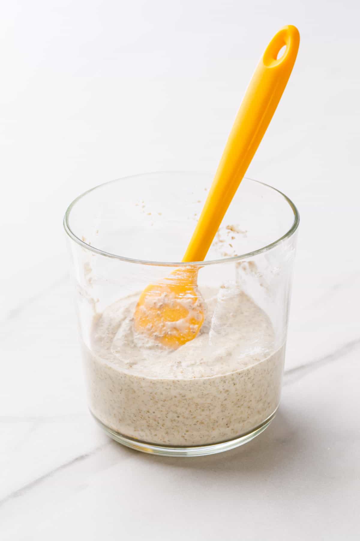 Sourdough Starter in a clear glass jar with a yellow silicone spatula. 