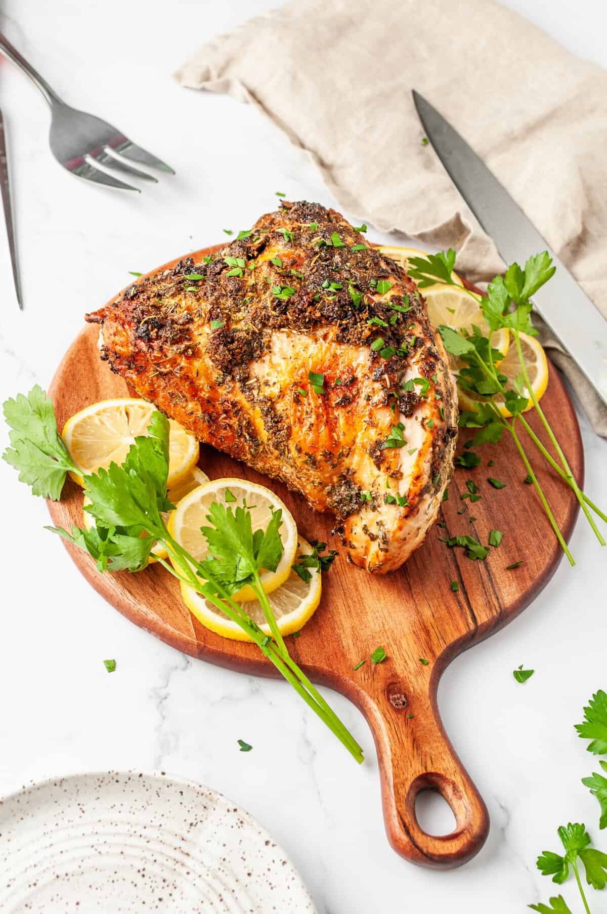 perfect air fryer turkey breast served on a round wooden board with lemon slices and parsley on the side
