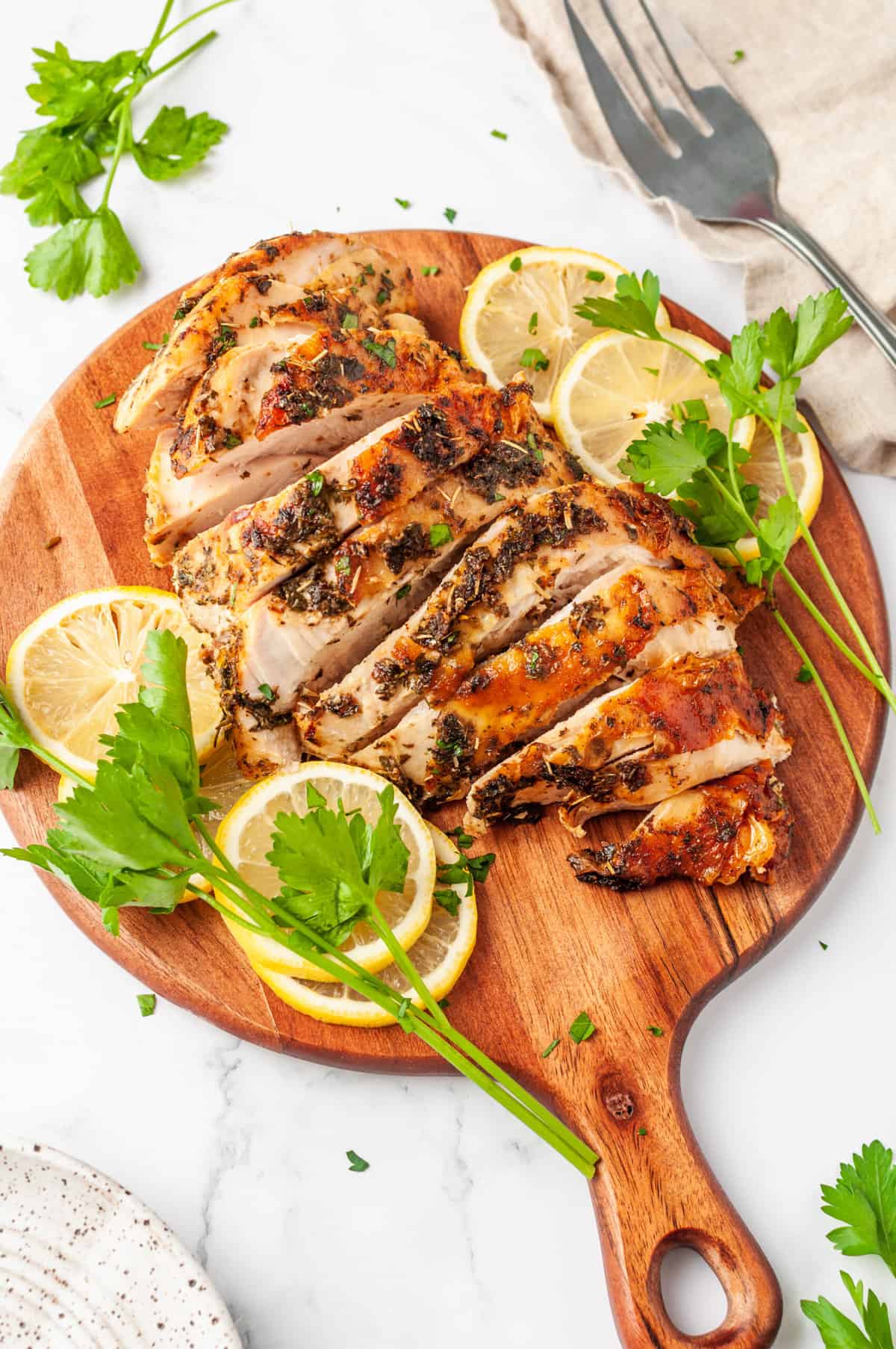 sliced air fryer turkey breast served on a wooden round board with lemon slices and parsley on the side