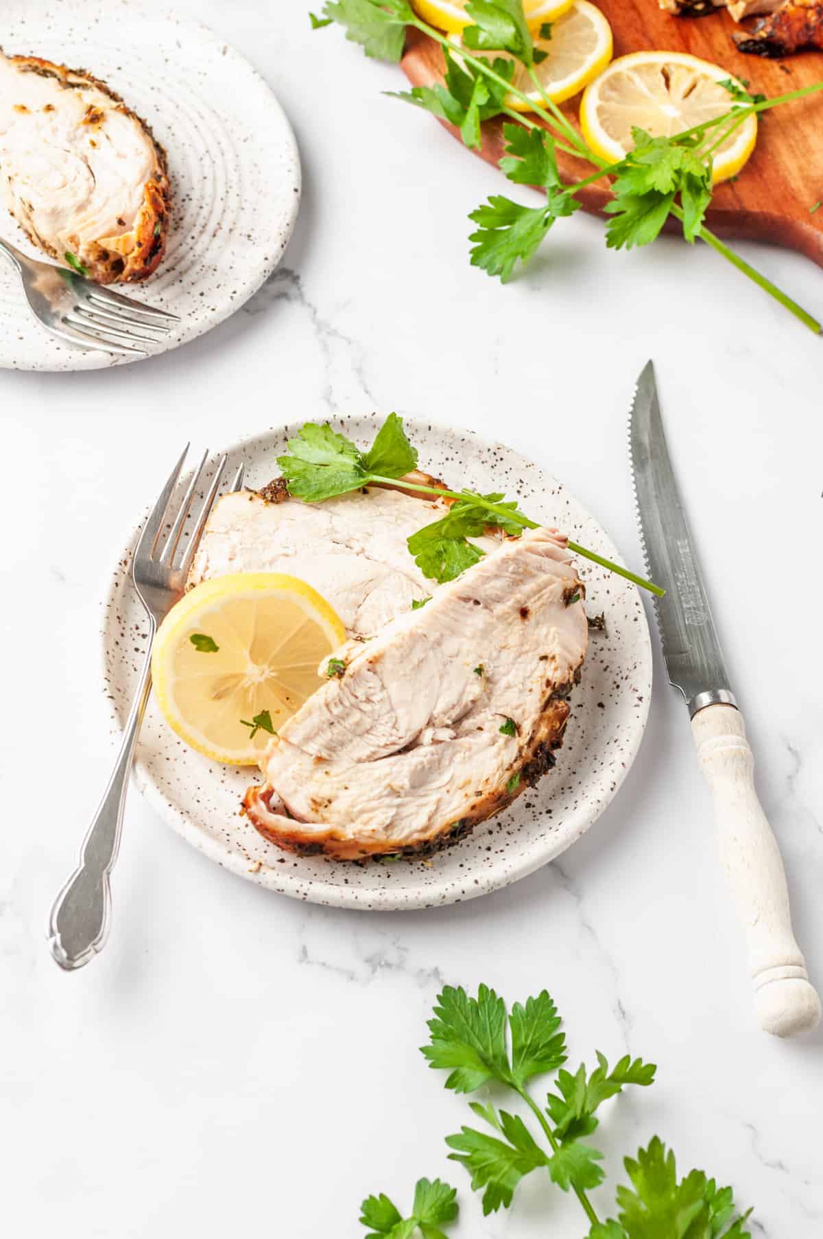 serving of air fryer turkey breast served on a speckled plate with a lemon slice and silver fork and knife