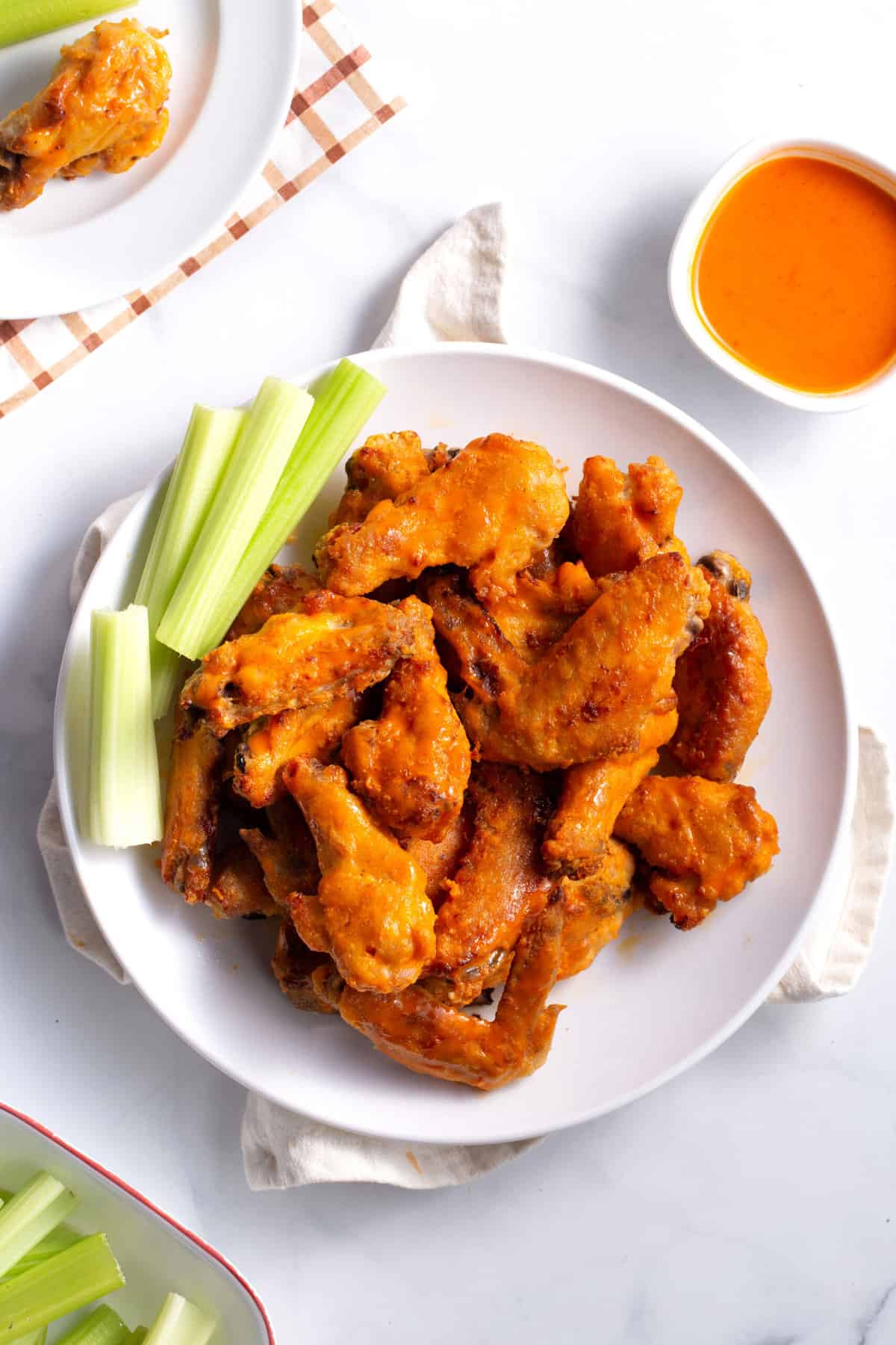 topped down image of baked buffalo wings served on a white round plate with a side of celery