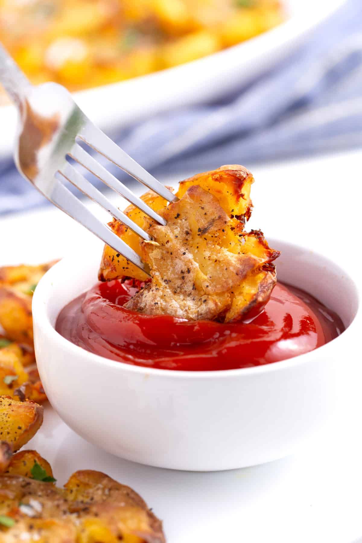 one crispy smashed potato on a fork dipping into ketchup