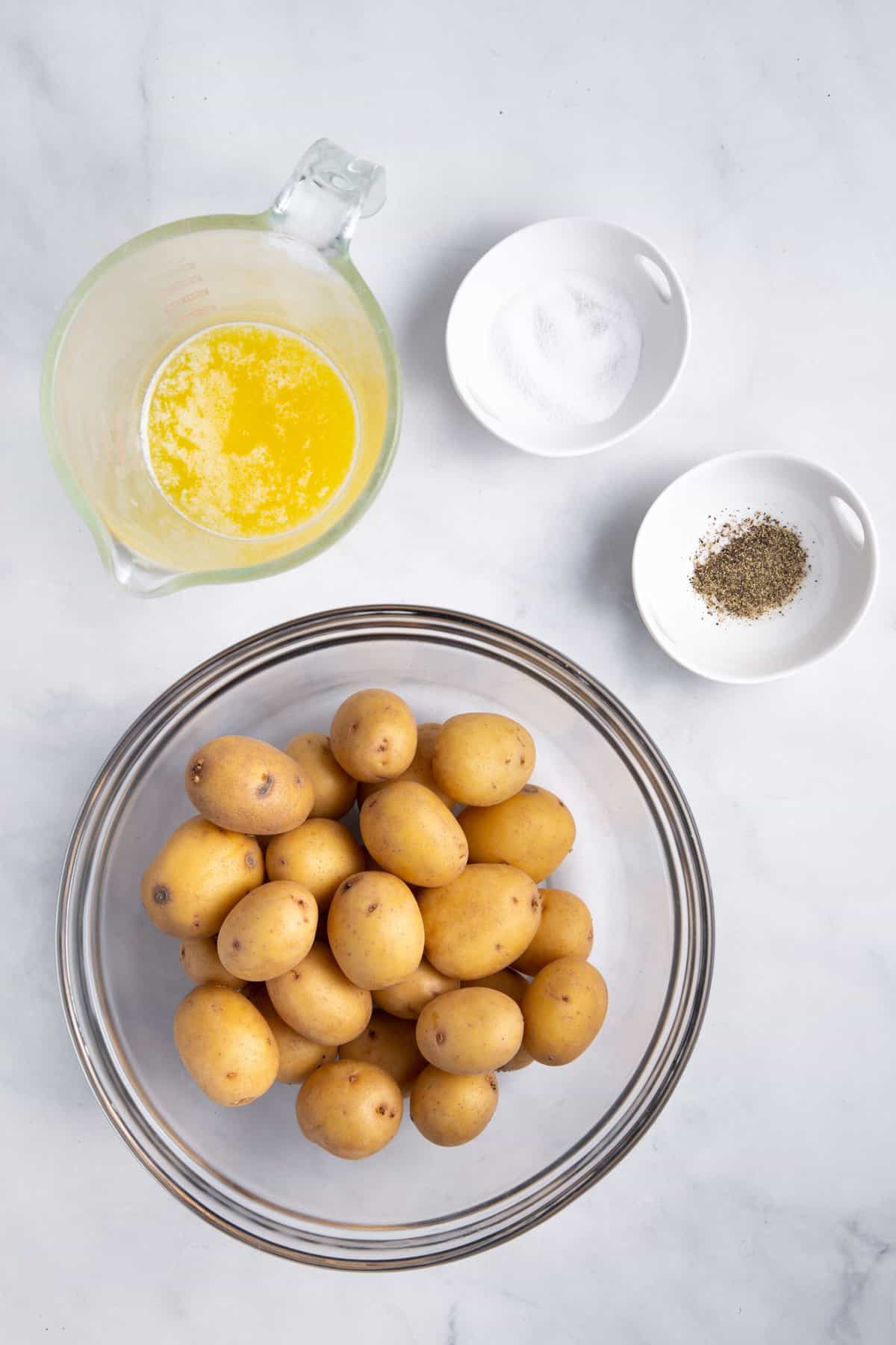 The ingredients needed to make crispy smashed potatoes are shown in bowls: butter, salt, pepper, and potatoes.