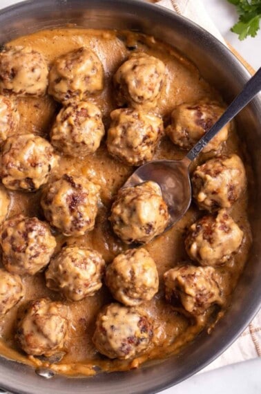 Swedish meatballs in a skillet with a spoon lifting one.