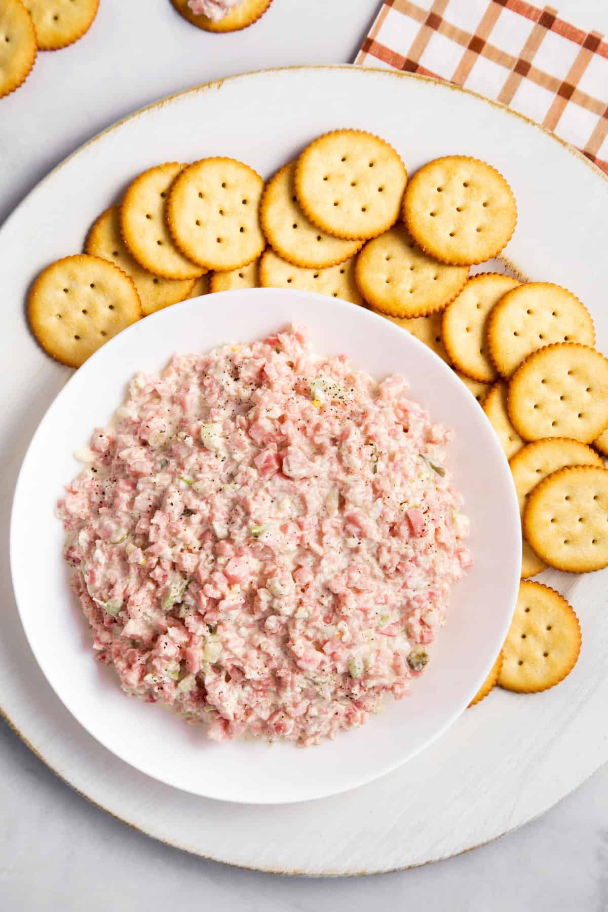 top down image of ham salad served in a large white bowel with rtiz crackers surrounding the bowl
