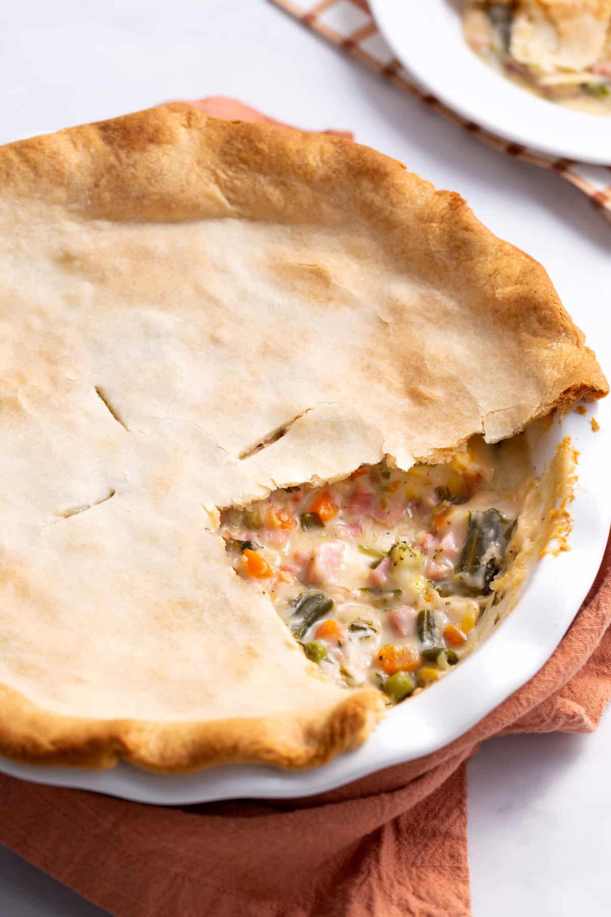 close up image of hot ham pie served in a pie dish with a slice cut out to show the interior.