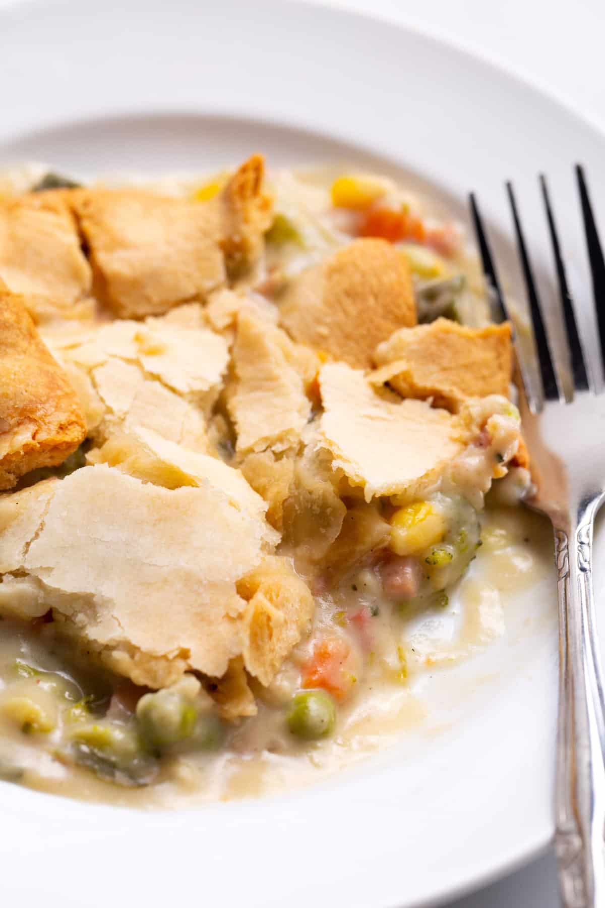 close up image of hot ham pie served on a white round plate with a silver fork.