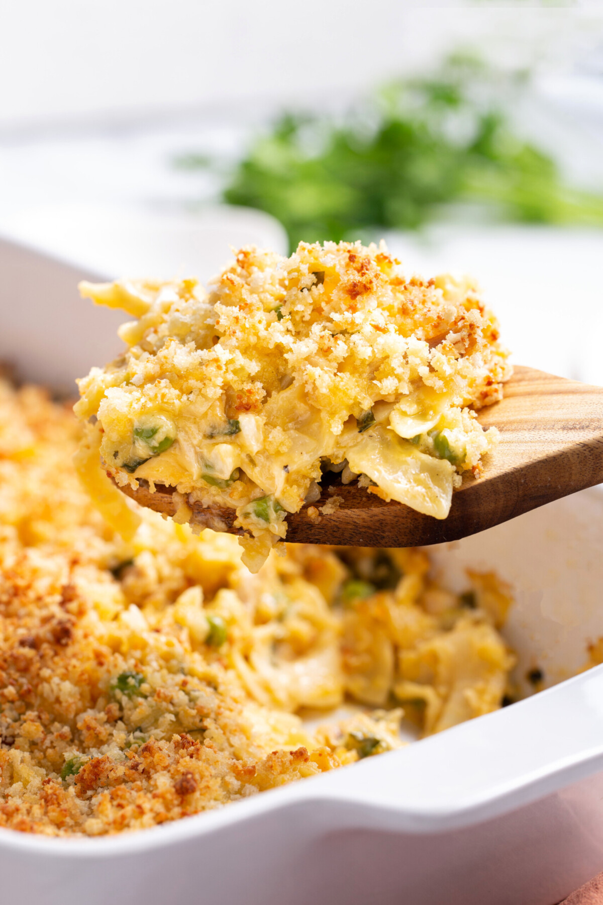 Leftover turkey casserole being scooped out of a baking dish on a wooden spoon.