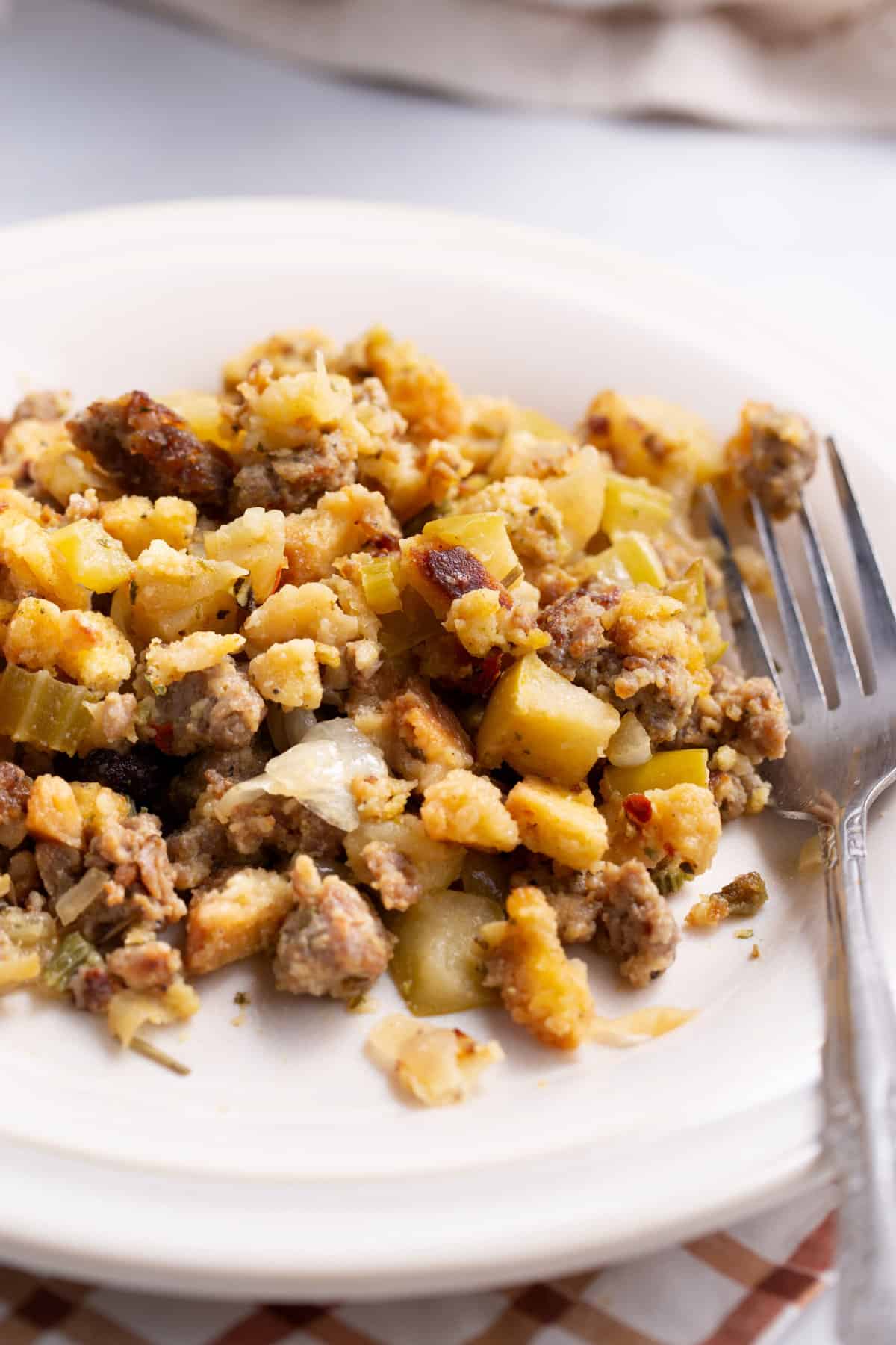 close up image of a serving of sausage and apple stuffing served on a white round plate with a silver fork